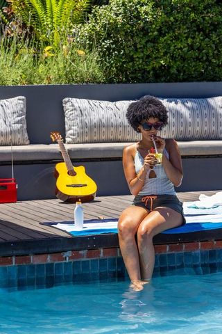 Black woman relaxing by pool with acoustic guitar and summer cocktail