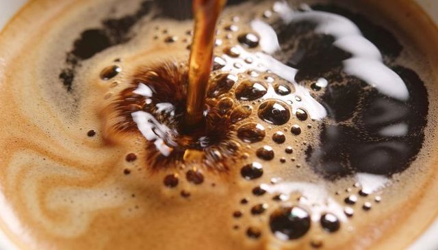 Pouring dark espresso creating rich crema and bubbles macro close-up of coffee surface