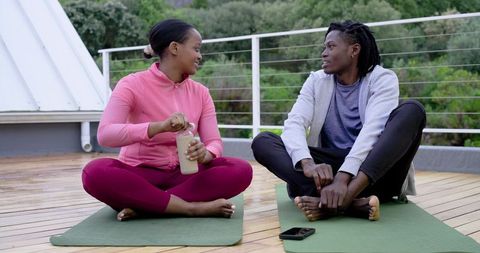 African American Couple Chatting and Hydrating on Rooftop Yoga Mats During Outdoor Workout
