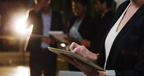 Businesswoman Tapping Tablet in Corporate Lounge with Team Collaborating in Background