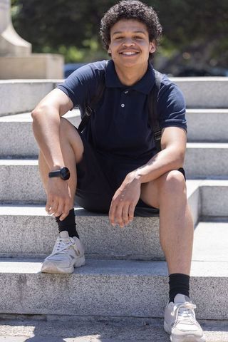 Young african american man sitting on stone steps smiling in navy polo and backpack