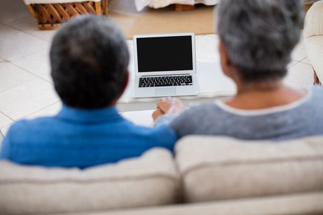 Senior couple holding hands while looking at the laptop at home