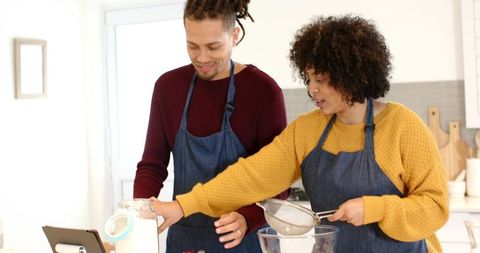 African American Couple Baking Together in Sunlit Kitchen Wearing Denim Aprons