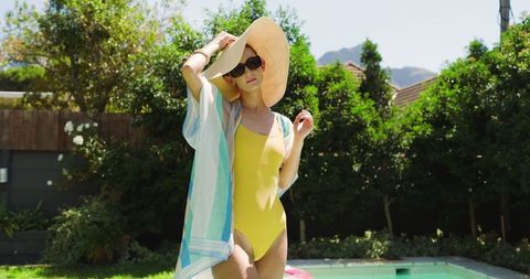 Stylish woman relaxing by backyard pool in yellow swimsuit