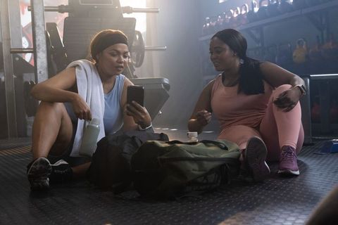 Diverse women taking break checking workout progress on smartphone while resting in gym