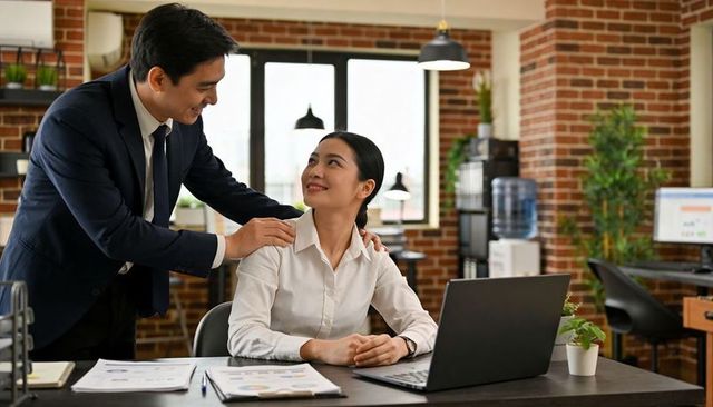 Manager placing hands on seated colleague shoulders in bright open-plan office