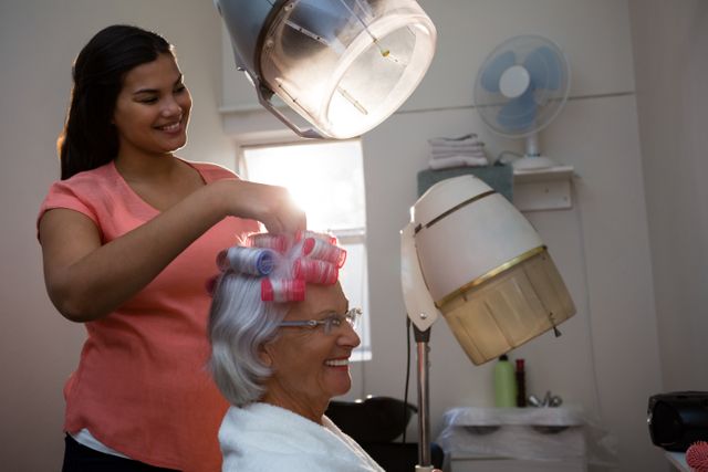 Smiling beautician removing curlers from senior woman hair at salon