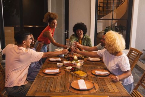 Friends toasting at candlelit patio dinner around wooden table with cheese platter