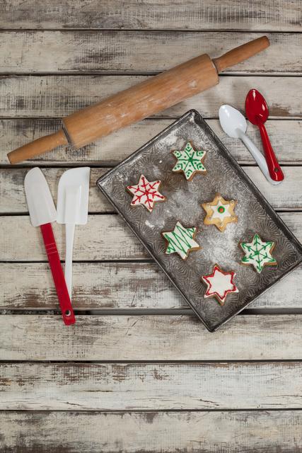 Spatula, spoon, rolling pin and tray with baked Christmas cookies kept on wooden table