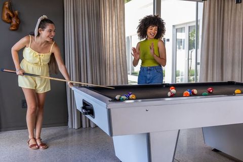 Friends playing pool in modern game room, laughing while taking shot