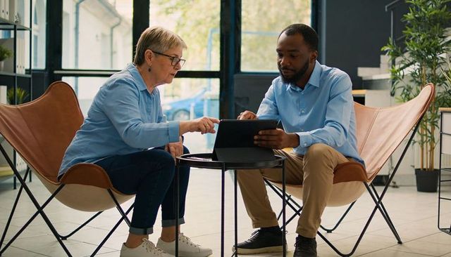 Senior woman mentoring colleague while reviewing tablet in modern office lounge