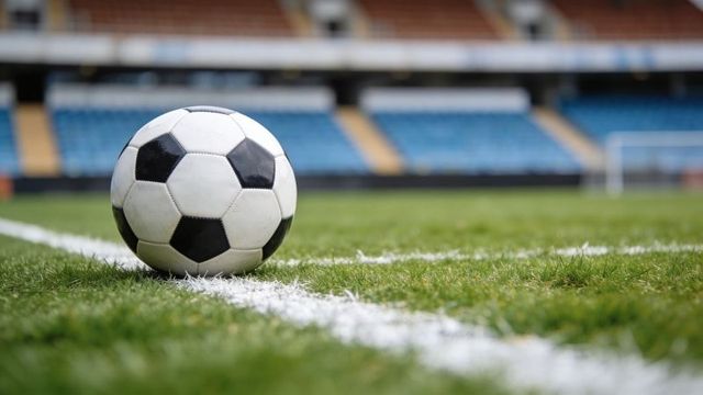 Soccer ball resting on white line at stadium pitch, low-angle closeup of turf and empty stands