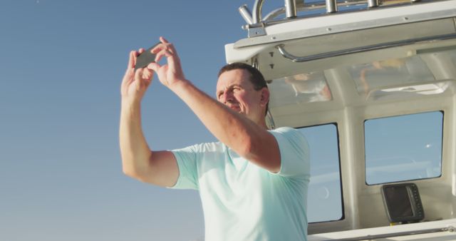 Happy caucasian man taking photo with smartphone on deck of small boat sailing on a sunny day. Leisure, hobbies, free time, travel and vacations.