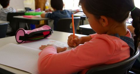 Young Schoolgirl Writing at Desk in Classroom - Download Free Stock Images Pikwizard.com