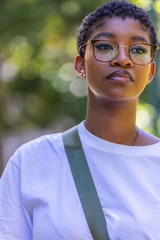 Sunlit african woman wearing glasses and white tee standing outdoors with thoughtful gaze