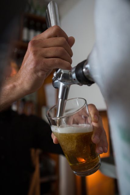 Mid-section of brewer filling beer in beer glass from beer pump in bar