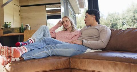 Young couple relaxing on leather sectional sofa chatting and enjoying cozy home weekend