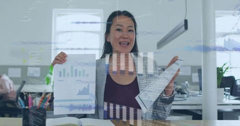 Korean businesswoman holding charts with digital analytics overlays in open office