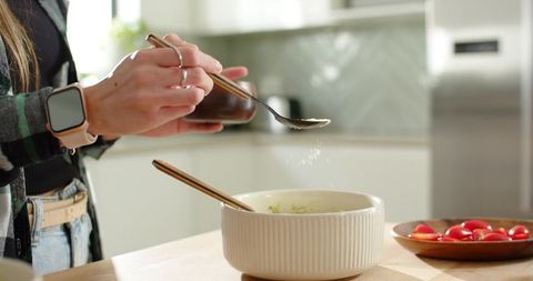 Sprinkling salt into ribbed mixing bowl while preparing fresh salad in modern kitchen