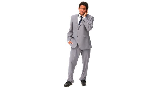 Young businessman dressed in a gray suit taking a phone call while standing against a white background. Suitable for corporate presentations, business communication themes, professional networking materials, and recruitment imagery.