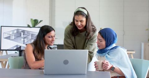 Asian female colleagues collaborating around laptop while reviewing 3d floor plan