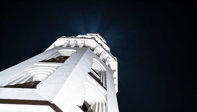 White stone tower rising at night with arched openings, dramatic uplighting, stars