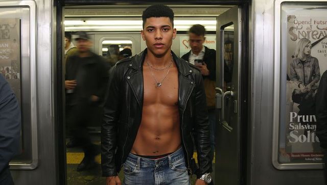Muscular shirtless man in subway doorway wearing leather jacket and silver chains, urban fashion