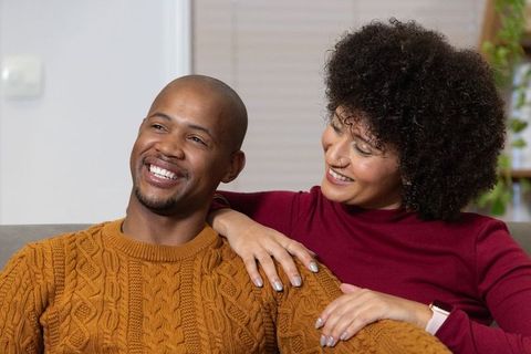 African american couple smiling on couch showing ring and watch, cozy home lifestyle
