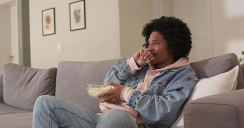 African american man watching movie on couch holding popcorn reacting to emotional scene