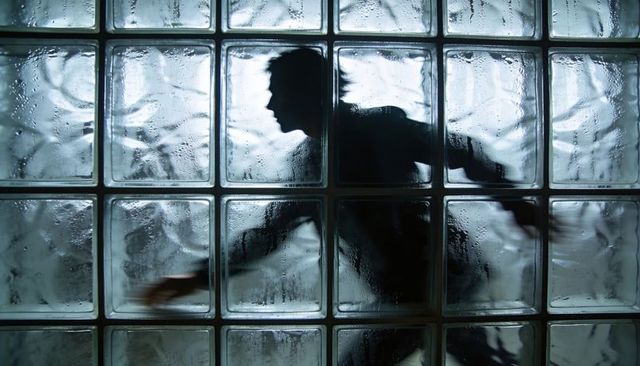 Male silhouette running behind glass block wall with condensation and dramatic backlight