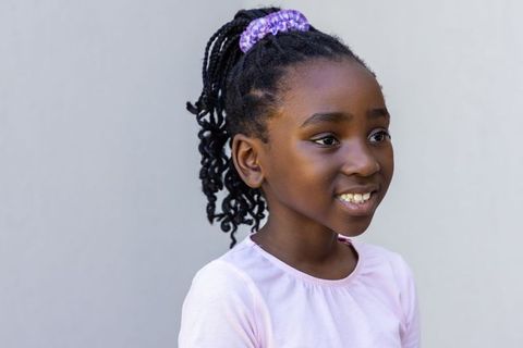 Young girl with braided ponytail and purple scrunchie smiling in pastel lilac outfit
