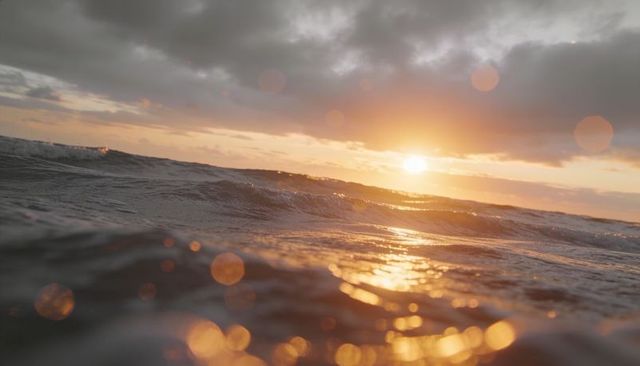 Sunset ocean waves reflecting golden light, rippling surf with bokeh flares and droplets