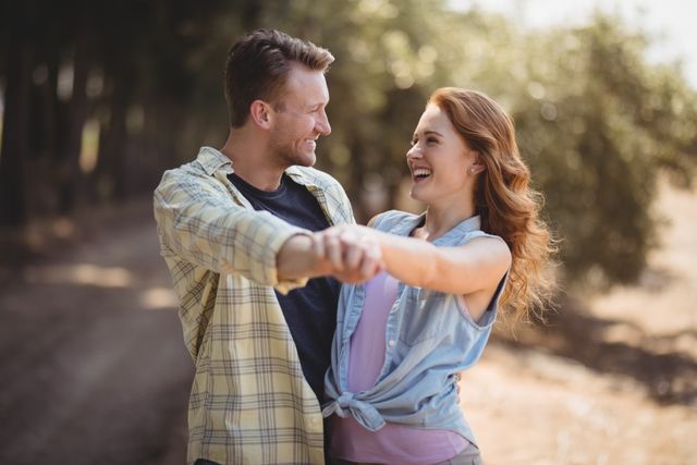 Young couple enjoying a sunny day at an olive farm, dancing and smiling. Perfect for themes related to love, romance, outdoor activities, and joyful moments. Ideal for use in advertisements, blogs, social media posts, and websites promoting relationships, nature, and lifestyle.