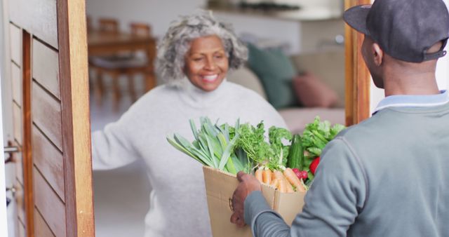 Happy senior african american woman receiving groceries from delivery man. Retirement and spending time at home concept.