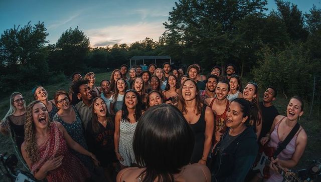 Large community choir singing together outdoors at sunset with guitars and joyful faces