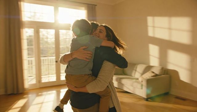 Mother hugging child in sunlit living room, celebrating new home with warm embrace
