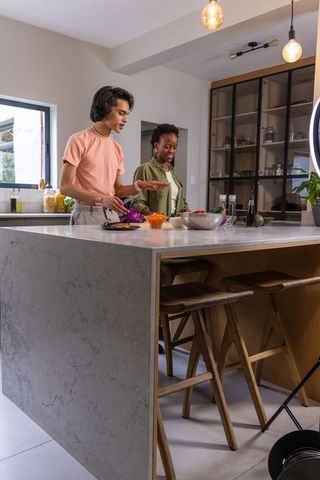 Multicultural couple preparing fresh salad on marble kitchen island in contemporary home