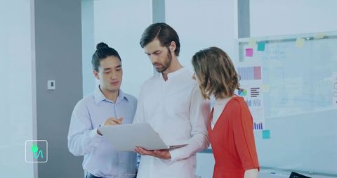 Team collaborating over laptop in modern office with glass whiteboard and charts