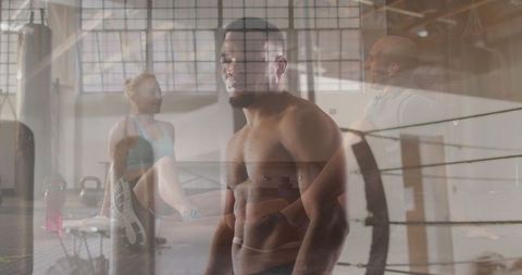 Muscular man in boxing gym with boxing equipment and trainer in background