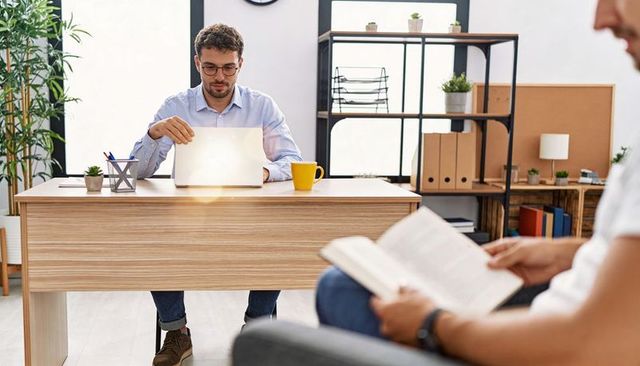 Focused young professional working on laptop at modern office desk with yellow mug