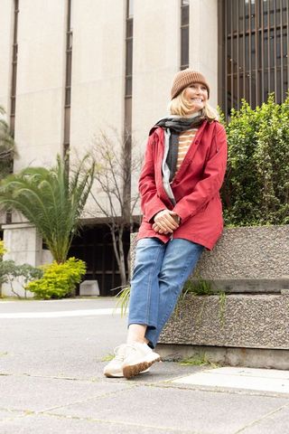 Smiling middle-aged woman sitting on urban planter wearing beanie, scarf and red jacket