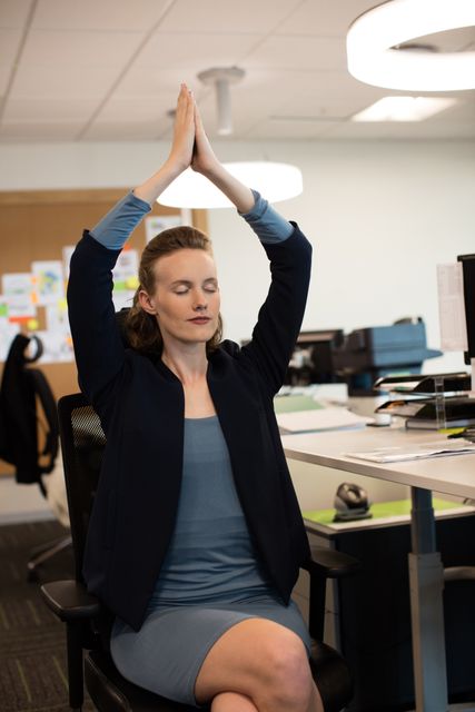Businesswoman practicing yoga while sitting on chair at office