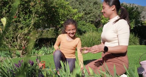 Parent and child gardening together in sunny backyard planting purple flowers and watering