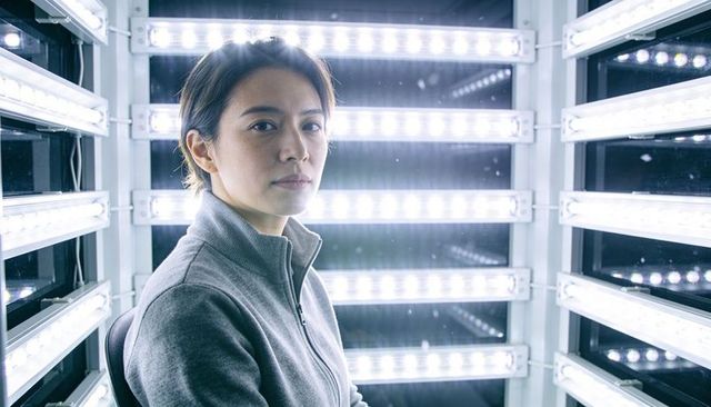 Woman sitting in led light booth wearing grey fleece facing camera with mirrored panels