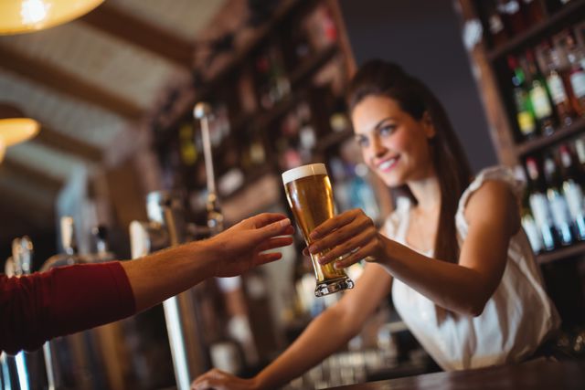 Female bar tender giving glass of beer to customer at bar counter