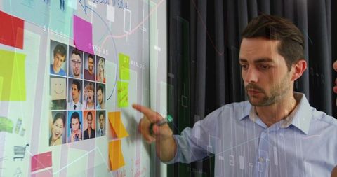 Reviewing team profile grid on glass whiteboard while planning campaign with sticky notes