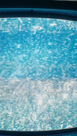 Closing in on oval porthole showing agitated turquoise water textures in vertical video