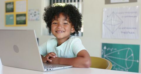 Smiling African American child using laptop in classroom with geometry posters diagrams