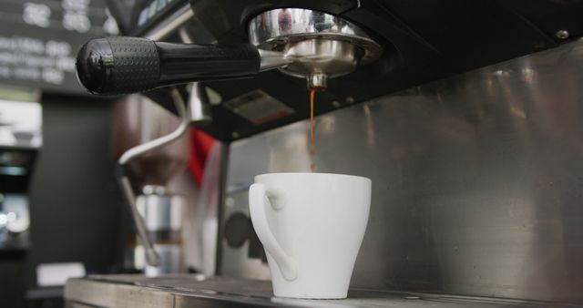 Close-up view of an espresso machine pouring fresh coffee into a white cup. Suitable for use in articles about coffee culture, barista training, coffee shop promotions, and beverage advertising.