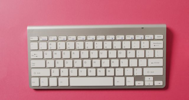 White wireless keyboard with sleek design against pink background. Ideal for office technology articles, workspace organization blogs, modern computing promotions, and design inspiring projects.